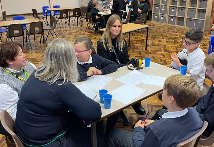 Primary aged children sit together with teachers at their multi schools council session