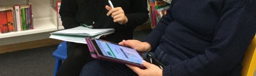 A shot of 2 people's hands and arms holding notepad, pen and iPad